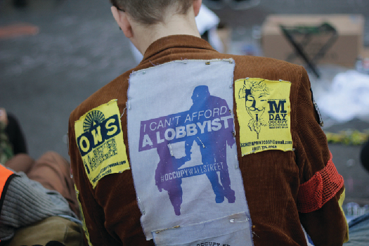 An image of the back a person wearing a jacket. A patch on the jacket reads “I can’t afford a lobbyist”.
