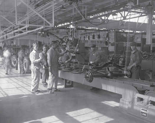 An image of a few people standing in an automotive plant next to some machinery.