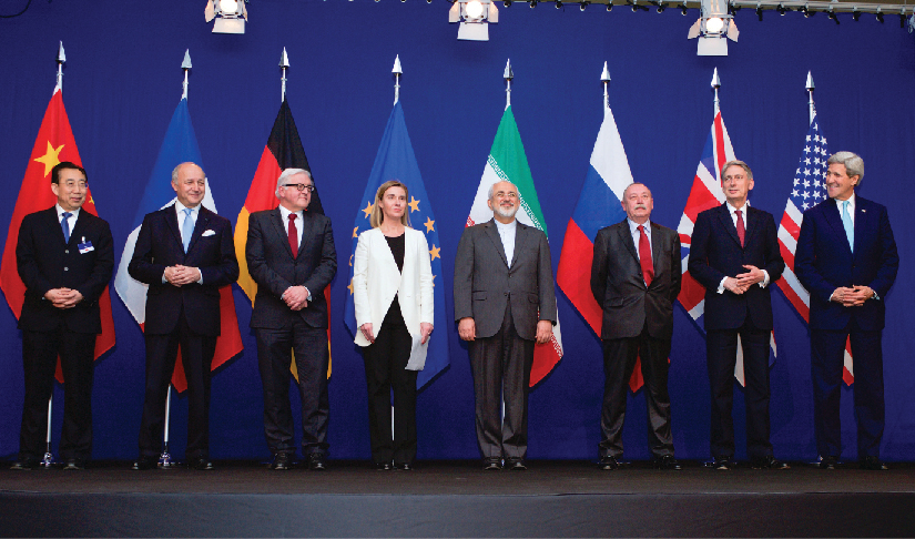 An image of the ministers of foreign affairs and other officials standing on a stage, each in front of the flag of their country.