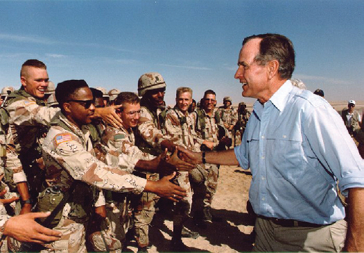 George H. W. Bush shaking hands with U.S. troops outdoors.