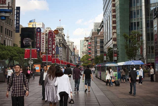 A busy street in Shanghai. Businesses, movie theaters, and restaurants line the sides of the street.