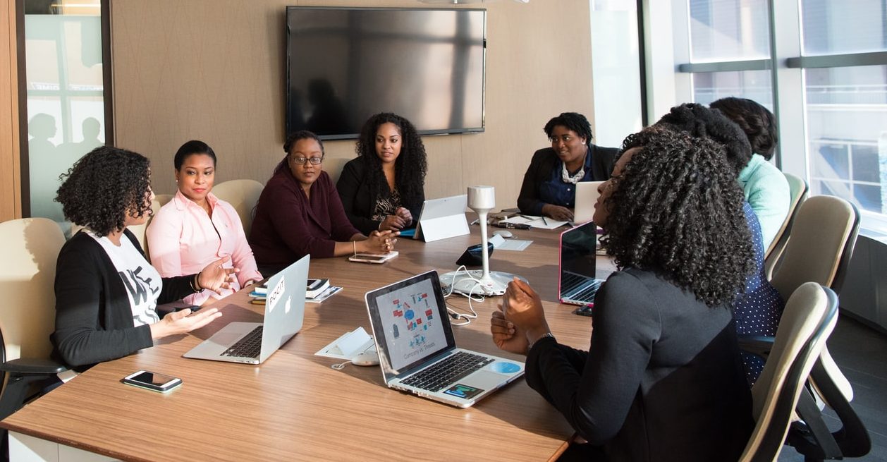 Eight women sit at a table in a meeting room.