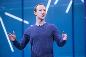 The founder of Facebook, Mark Zuckerberg, gives a speech. Behind him is a blue background.