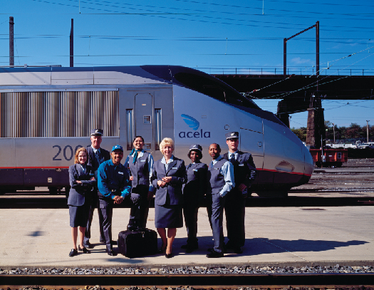 A photo of Amtrak staff standing on a train platform as a train passes behind them.