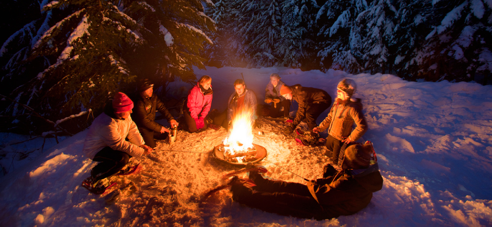 Photograph of people sitting around a campfire in the snow.