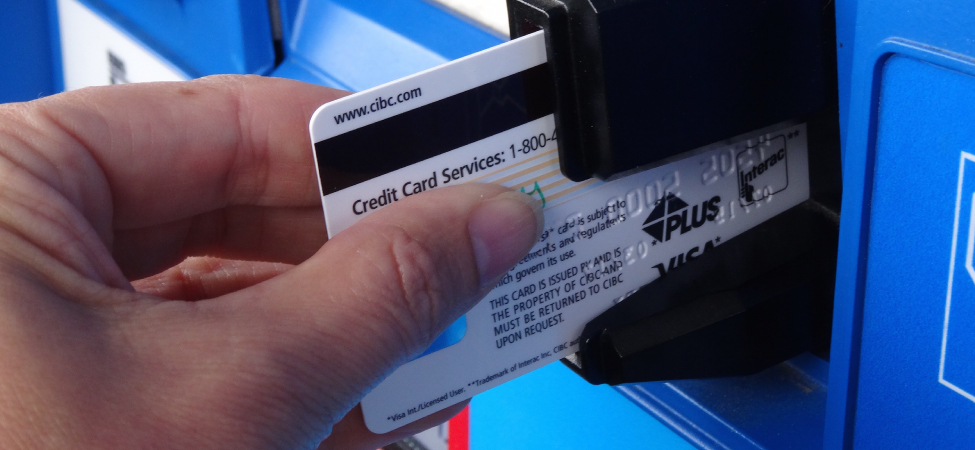 Figure is the photo of the credit card inserted half-way into the slot of the banking machine so that the black magnetic strip is visible.