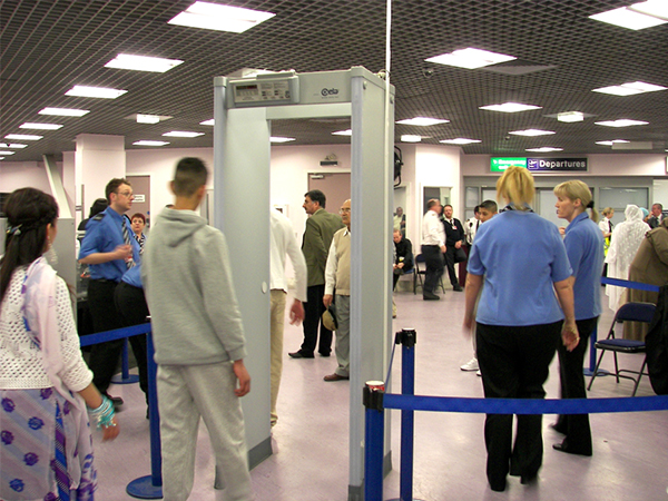 Photograph of people queued up at a metal detector gate at an airport.