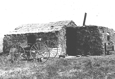 A photograph shows a sod house with a wagon in front of it.