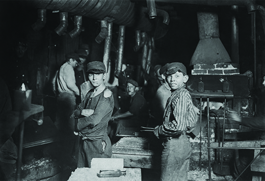 A photograph shows a small group of children working in a factory. Two boys, with tattered clothes and dirt-smudged faces, stand in the forefront.