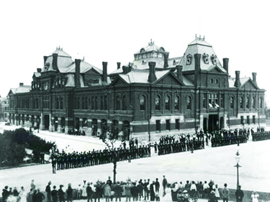 alt="A photograph shows a long line of strikers facing a long line of Illinois National Guardsmen in front of a railroad building."