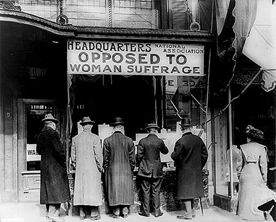 A photograph shows five men and a woman standing outside of a building labeled "Headquarters National Association Opposed To Woman Suffrage."