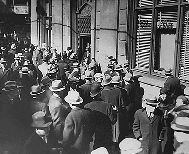 A photograph shows a large crowd of men and women waiting outside of a bank.