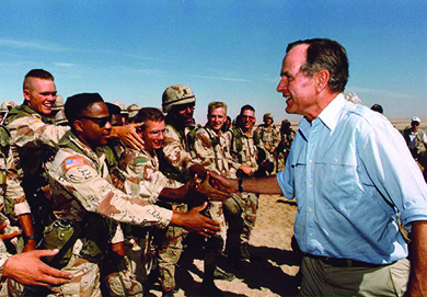 A photograph shows George H. W. Bush greeting and shaking hands with U.S. troops stationed in Saudi Arabia.