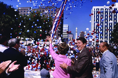 A photograph shows Ronald and Nancy Reagan on the campaign trail. They stand amidst a cheering crowd, surrounded by red, white, and blue balloons. Nancy Reagan waves to the crowd; Ronald Reagan smiles and places a hand on her back.