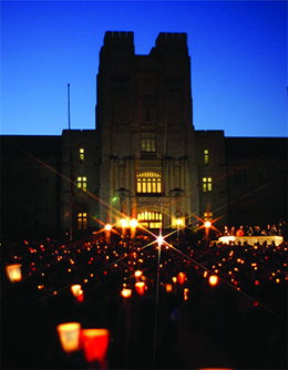 A photograph shows a massive crowd gathered in darkness in front of a large university building, holding candles.