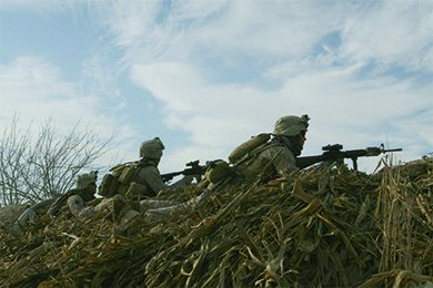 A photograph shows several Marines in position behind a hill, with their guns poised for attack.
