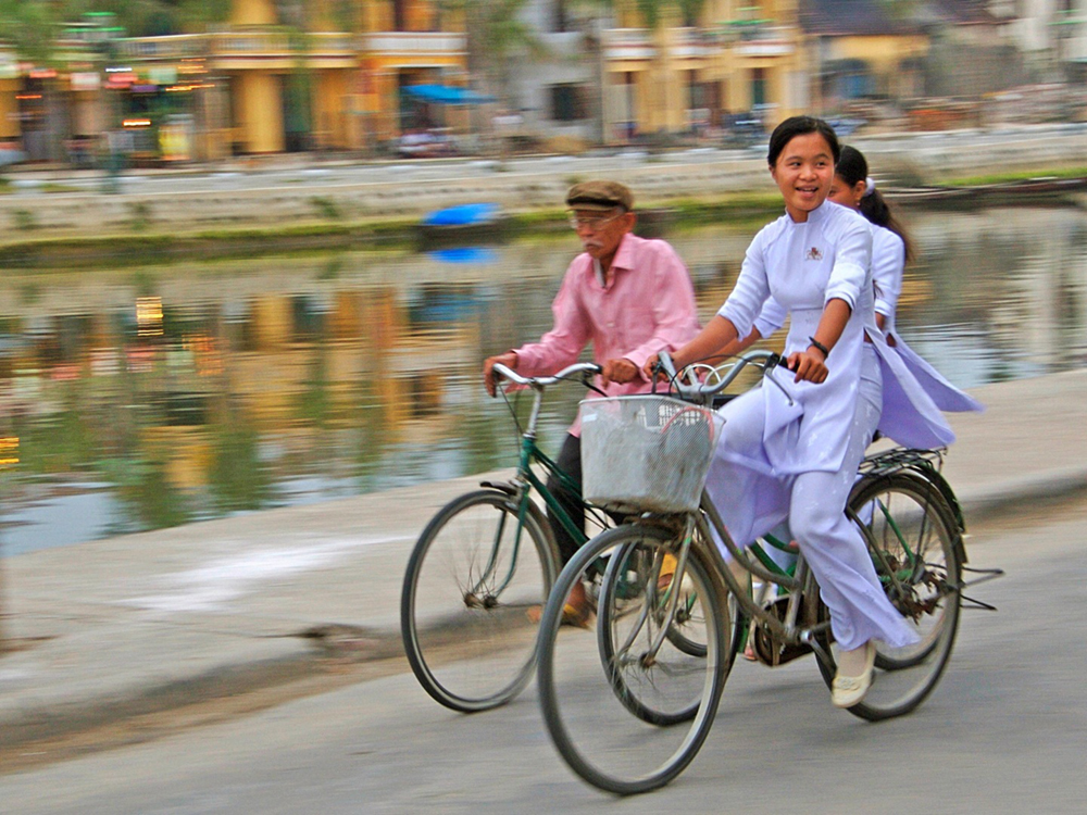 Three people cycling along a canal. The blurred buildings in the background convey a sense of motion of the cyclists.