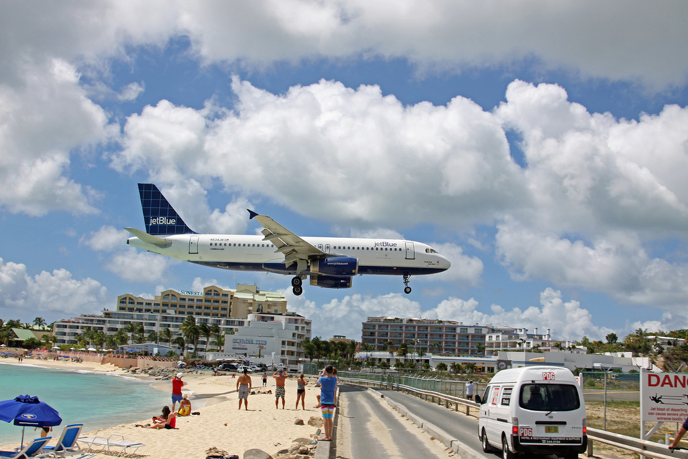 An airplane flying very low to the ground, just above a beach full of onlookers, as it comes in for a landing.