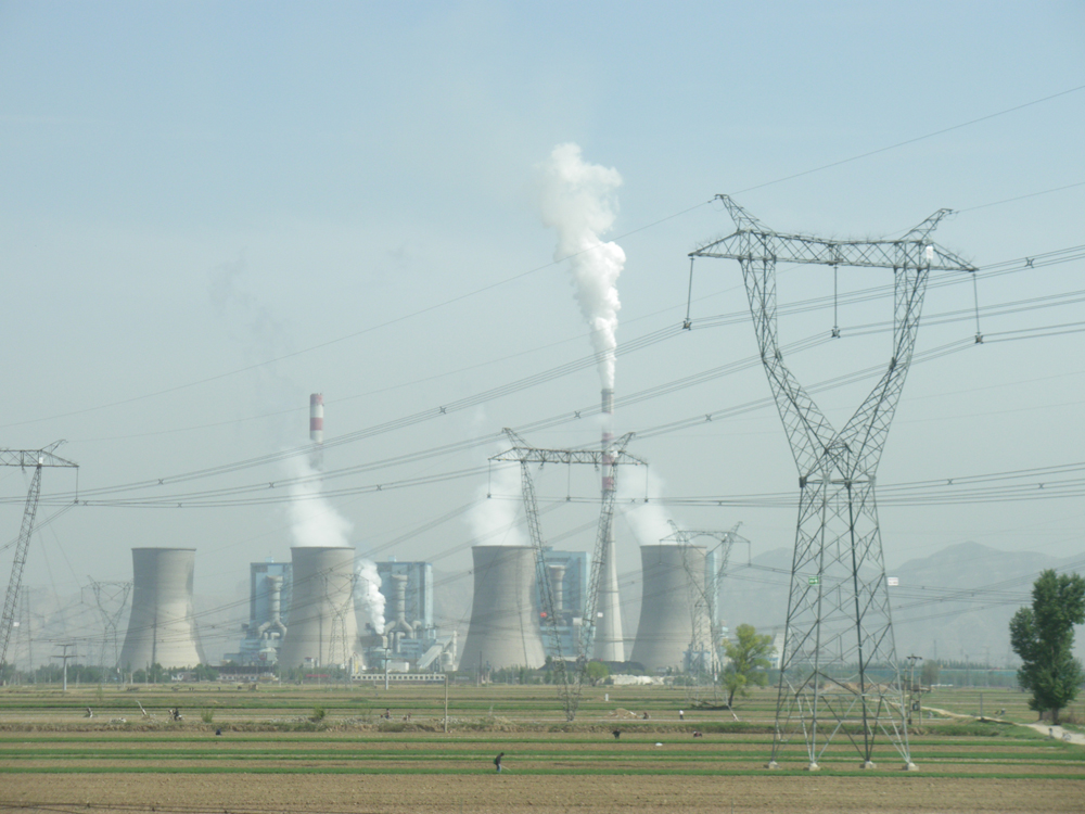 A distant view of a coal-fired power plant with clearly visible cooling towers generating electric power and emitting a large amount of gases.