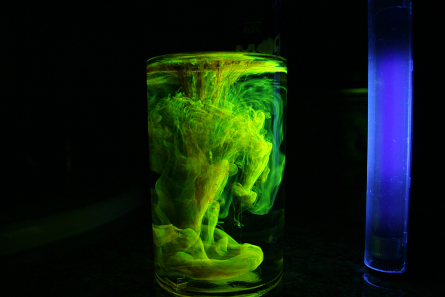 A beaker of water in which fluorescent powder is added. Near the beaker an ultraviolet light source is placed. In this ultraviolet light, the fluorescent powder in the water glows like green smoke.