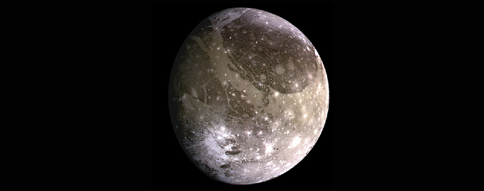 Photograph of Jupiter’s moon Ganymede. This image shows nearly the entire disk of Ganymede. The surface is covered with brown and gray rocky areas, and many craters that are nearly the same color as the surface. Below and to the right of center are many bright, rayed craters due to recent impacts that have exposed fresh ice from below the surface.
