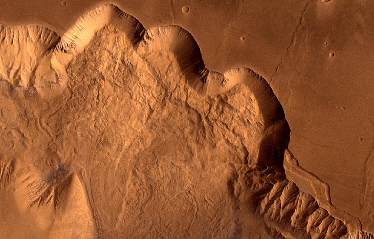 Erosion on Mars. The sloped valley wall winds its way across this image from the upper left section to lower right section while separating the flat plains above and the debris covered valley floor below.