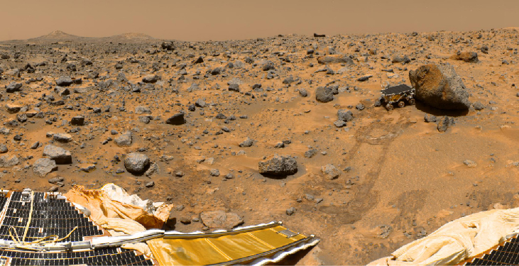 Surface view from Mars Pathfinder. At the lower left in this image, a portion of the lander and the ramp used to deploy the Sojourner rover is seen. Tracks lead away from the ramp to the large boulder at the upper right of this image. The rover is positioned immediately to the left of the boulder.