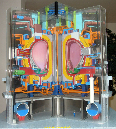 Cutaway Model of the ITER Design. In the center of this model are two pink kidney shaped areas that represents the hollow chamber wherein the particles will travel. The bright yellow areas surrounding the chamber are the superconducting magnets. Surrounding these two structures are a myriad of pipes, wires, conduits and other components of this highly complex machine.