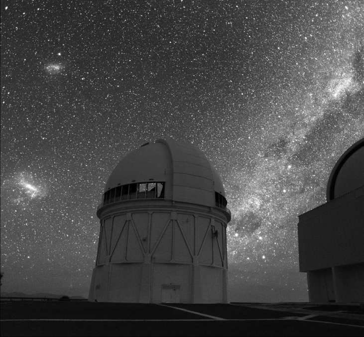 Photograph of the 4-meter telescope at Cerro Tololo Inter-American Observatory silhouetted against the southern sky. The Milky Way is seen to the right of the dome. The Large and Small Magellanic Clouds are seen to the left.