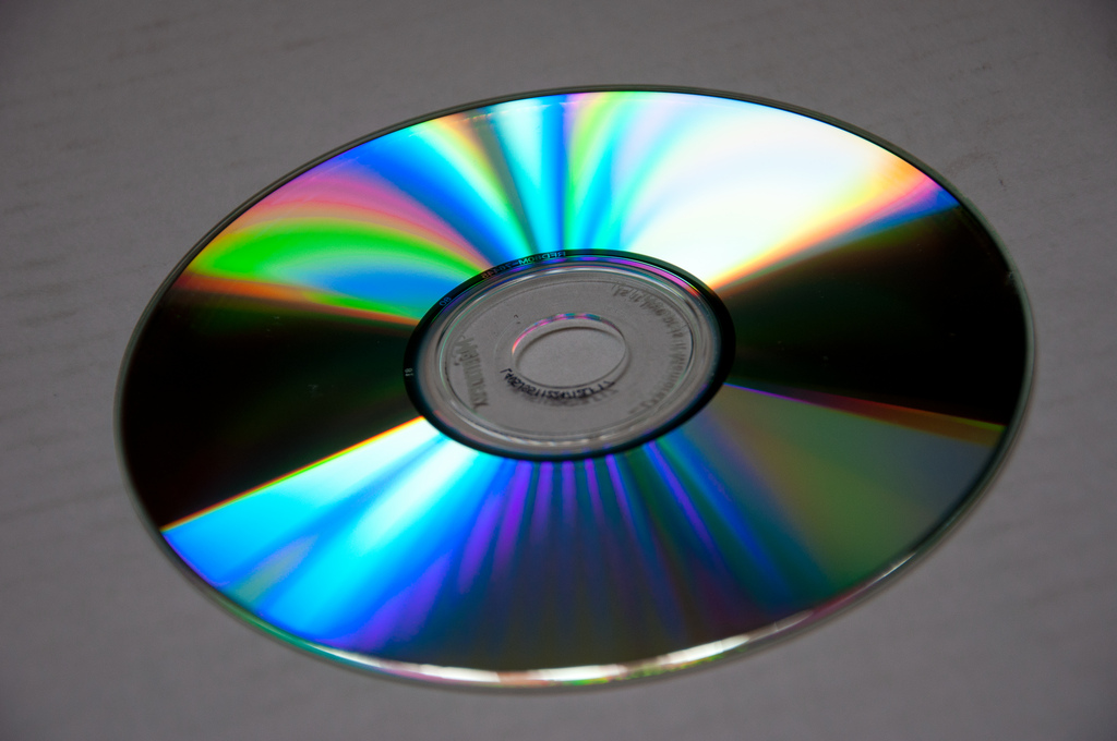 Photograph of the reflective side of a C D. Regions of the disc reflect a rainbow of colors.