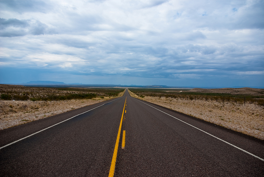 A long isolated double-lane road banked by barren land on both sides.