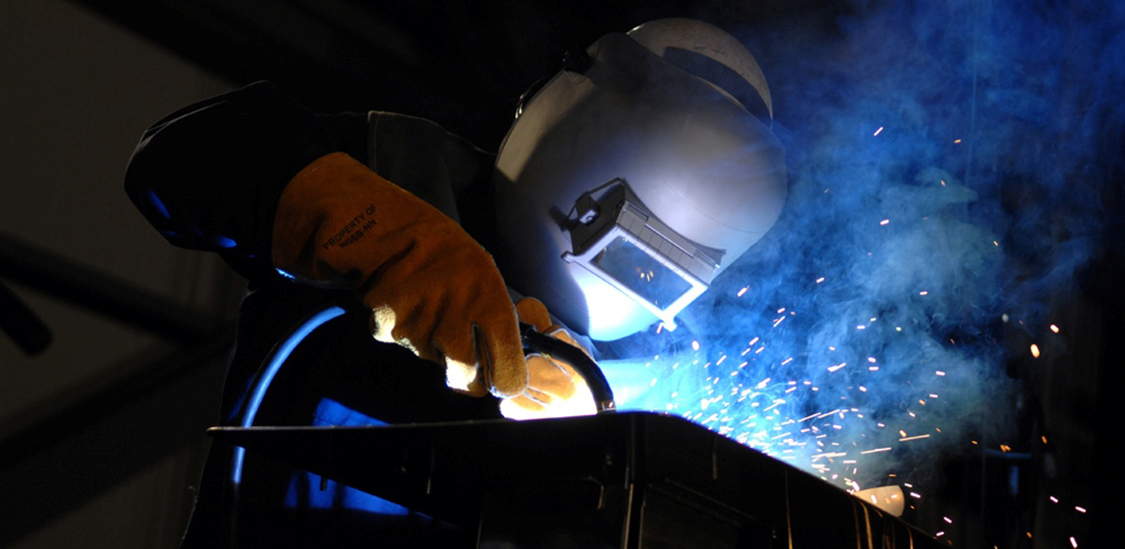 Photograph of a welder wearing protective gloves and helmet, engaged in the task of welding.