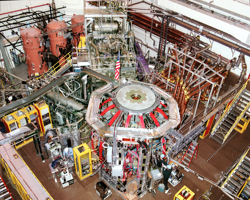 This photo shows the outside of the fusion reactor of the National Spherical Torus Experiment at the Princeton Plasma Physics Laboratory. The reactor, which sits in a large room, is connected to numerous tubes and instruments.