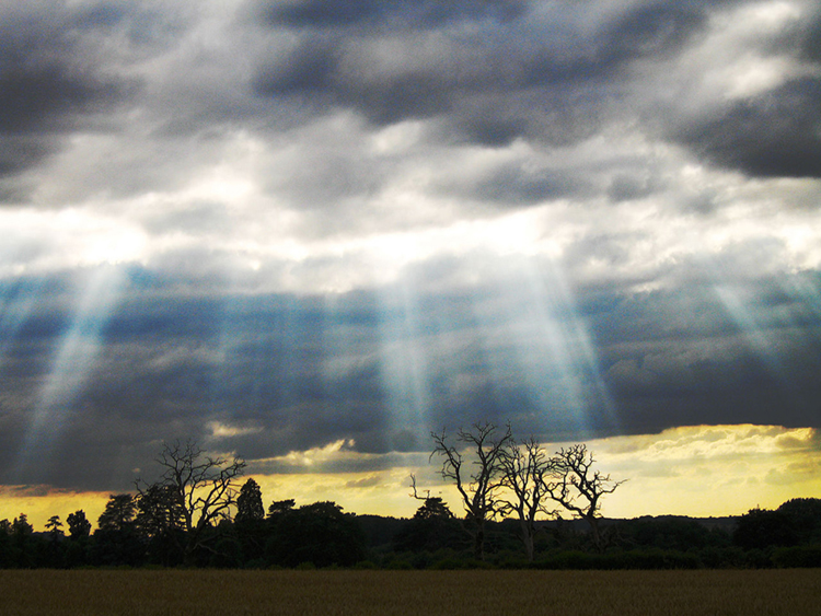 This figure shows Sun rays piercing clouds to illuminate a natural scene.