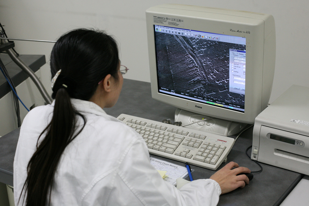 Image shows the front view of a desktop computer along with a keyboard and printer with an image being displayed on the computer screen. It also depicts the back of a woman holding the mouse.